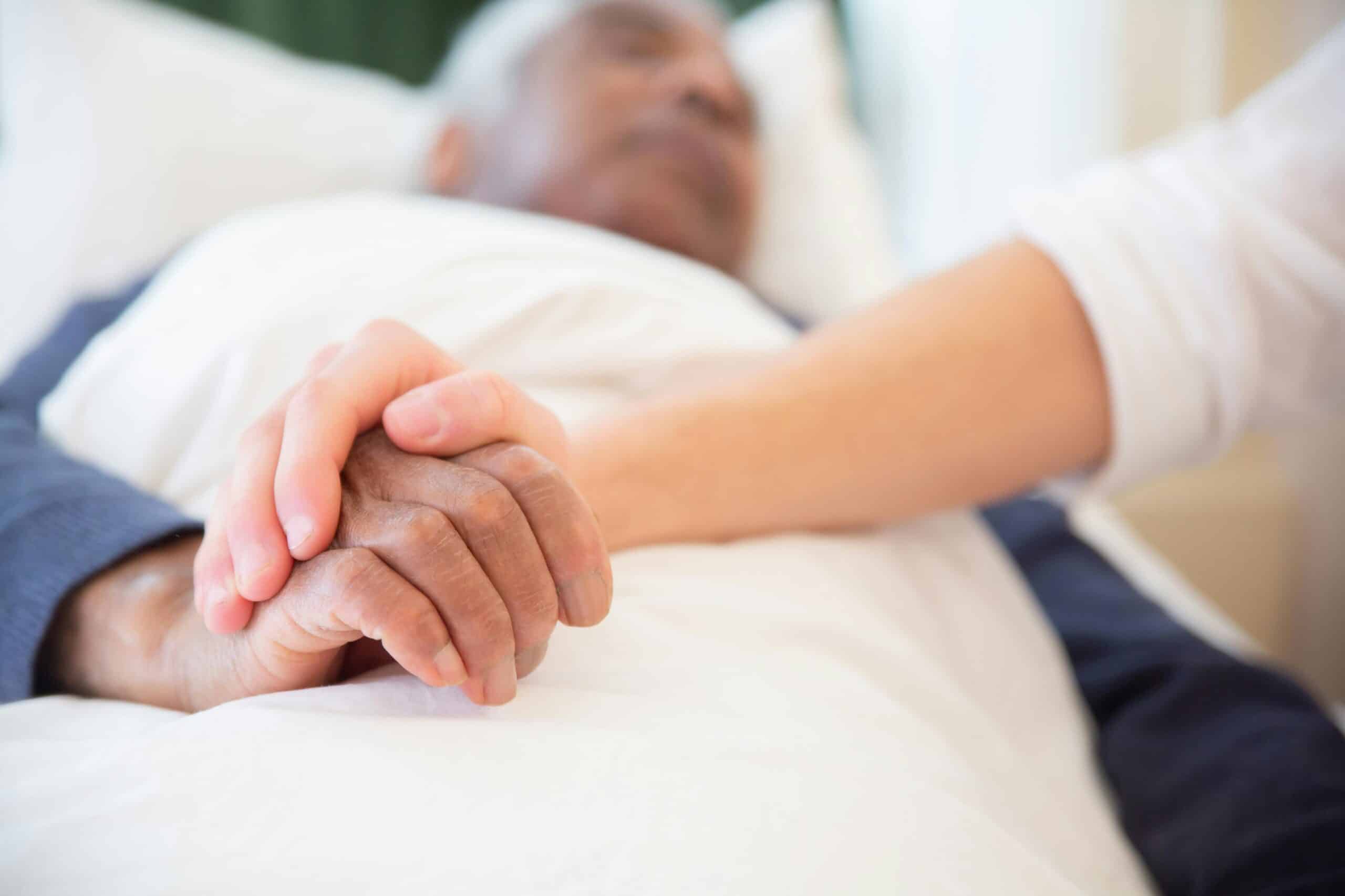 senior man holding a hospice or palliative care nurse's hand